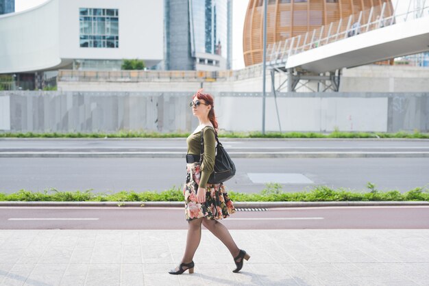 Lado completo de pin joven hermosa chica pelirroja paseando al aire libre en la ciudad, con vistas