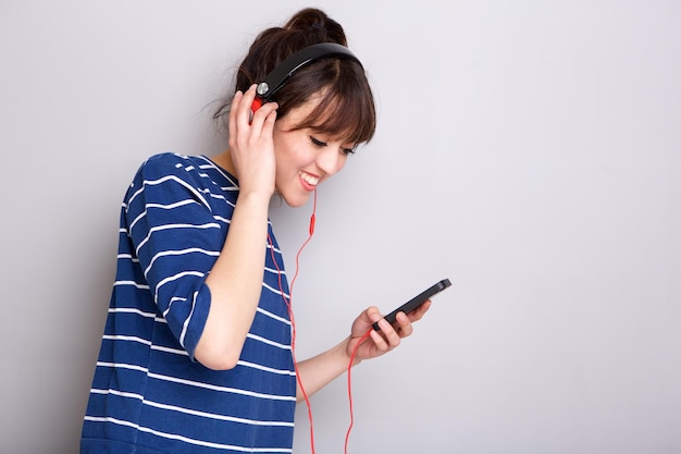 Lado de jovem ouvindo música com fones de ouvido e telefone celular contra a parede cinzenta
