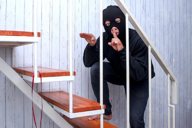Ladrão mascarado ou intruso de casa usa balaclava na cabeça entrando furtivamente em casa à noite em pé