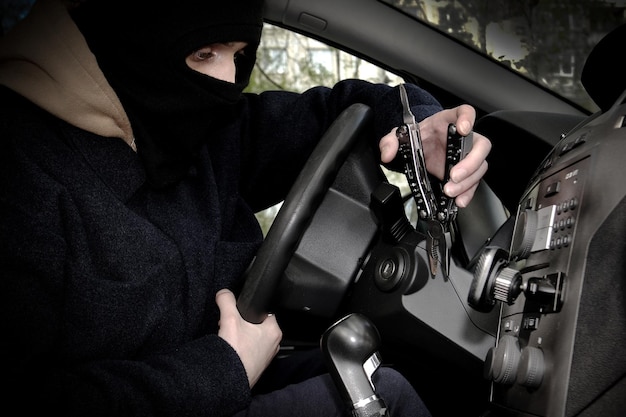 Un ladrón de autos está tratando de abrir la cerradura de encendido con una herramienta El ladrón de autos escondió su rostro en un pasamontañas
