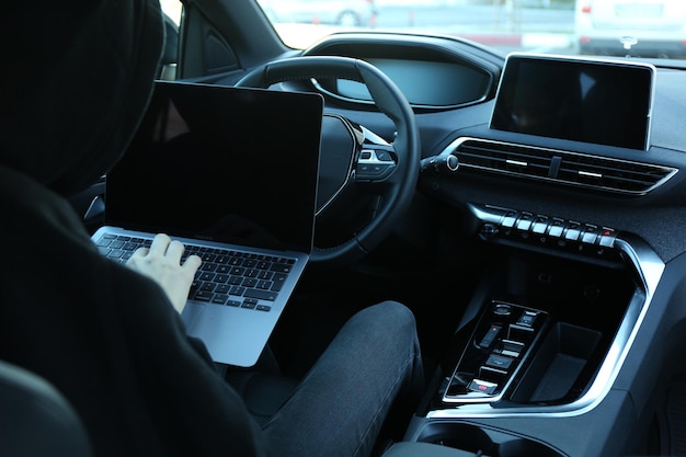 Un ladrón hackeando el sistema del coche con una computadora portátil dentro del vehículo en primer plano