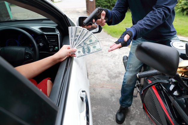 Ladrón con pistola en motocicleta robando dinero de mujer en el auto