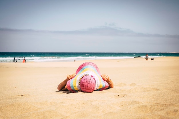 Lady deitou-se na praia na areia aproveitando o sol e o clima em férias em um chapéu rosa de resort de ilha tropical para proteger a pele do conceito de estilo de vida de viagem ao ar livre uva solar