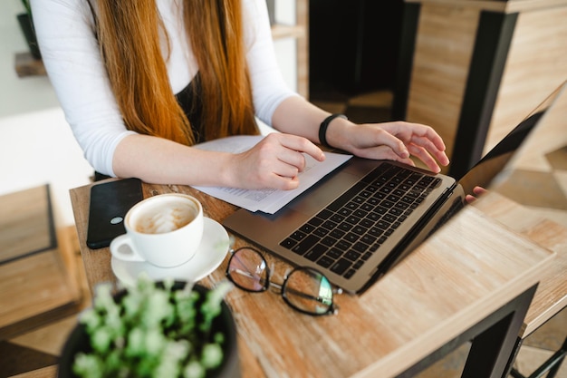 Lady freelancer trabaja en la computadora portátil y bebe café en una cafetería Trabajando en un fondo de café