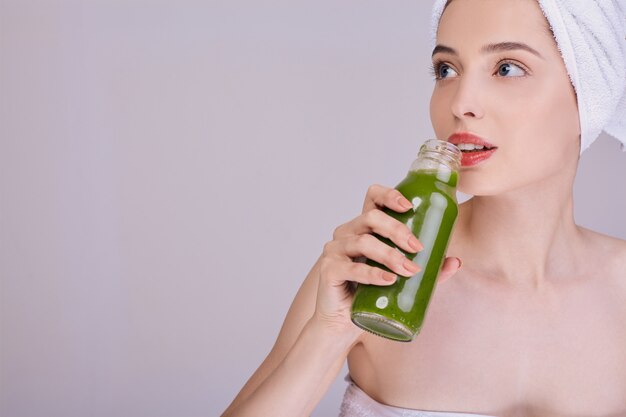 Lady genießt nach dem Duschen einen grünen Smoothie in einer Flasche.