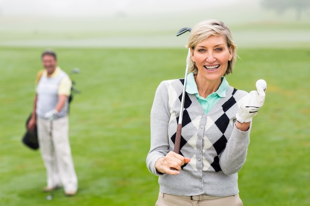 Lady golfista sorrindo na câmera com parceiro atrás