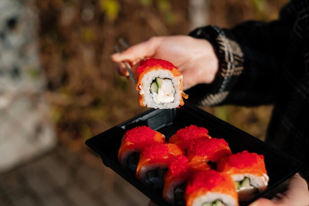 Lady leva sushi com pauzinhos de uma caixa para viagem