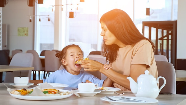 Lady Mama hält Pizzastück und Tochter isst im Café