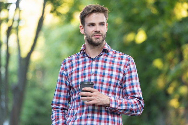 Lächeln des jungen Mannes im karierten Hemd mit Kaffeetasse