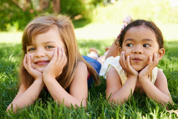 Foto lächeln natur und porträt von kindern auf dem gras spielen zusammen im freiluftpark oder garten im urlaub glückliche bindung und junge mädchen kind freunde entspannen auf dem rasen auf dem feld im urlaub oder wochenende