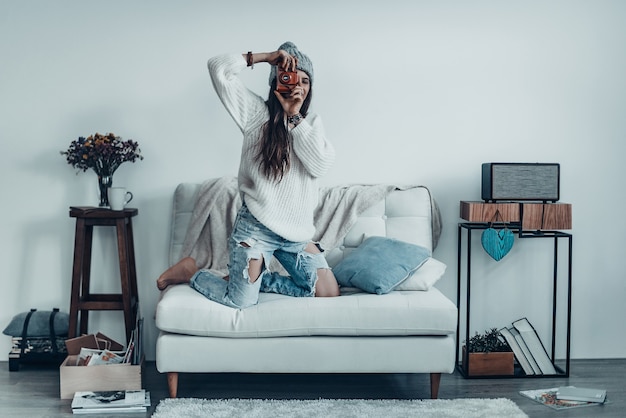 Lächeln! Schöne junge Frau in Freizeitkleidung und Strickmütze, die ein Foto von ihrer Retro-Kamera macht