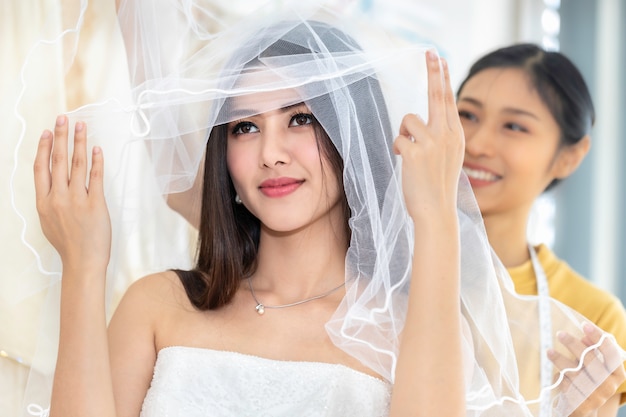 Lächeln Sie asiatische Frau, die auf Hochzeitskleid in einem Geschäft durch den Schneider misst.