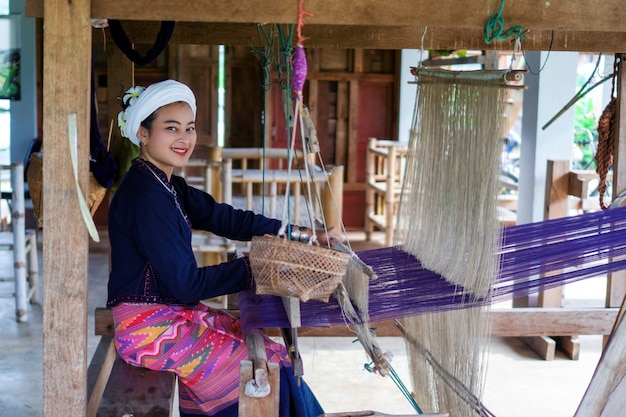 Lächeln Sie asiatische Frau in Tai Lue traditioneller Kleidung (Kultur des Nordens Thailands), die Stoff mit alter Holzmaschine webt