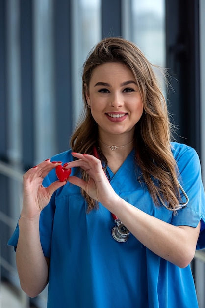 Lächeln Sie hübsche Ärztin in blauer Uniform mit dem Stethoskop, das Herz hält. Gesundheitspflege