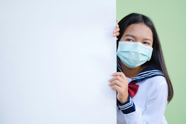 Lächeln Sie junges Mädchen tragen Maske mit Bulletin Board, grüner Hintergrund, asiatisches Mädchen.