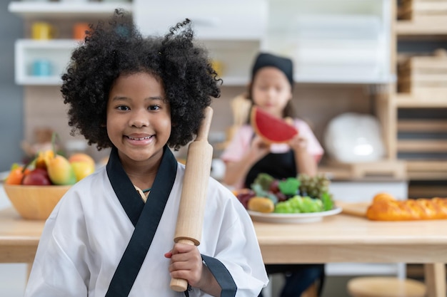Lächeln Sie kleines Mädchen in Kochuniform, das Nudelholz hält, um sich darauf vorzubereiten, Kuchenbäckerei in der Küche zu machen