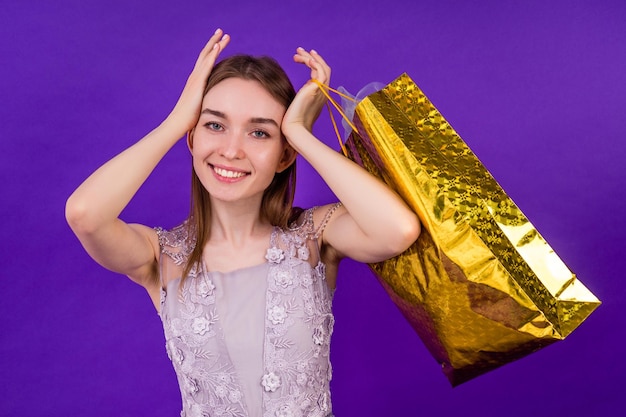 Lächeln überrascht schöne Frau shopaholic mit Make-up mit Einkaufstüten im Studio auf violettem Hintergrund.