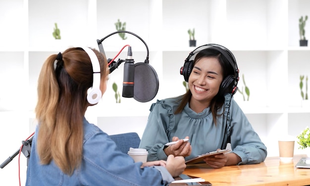 Lächeln zwei asiatische junge Frau Mann Radiomoderatoren im Kopfhörermikrofon, während Gesprächsaufnahme Podcast im Rundfunk im Studio zusammen sprechen Technologie zur Herstellung von Audiokonzepten