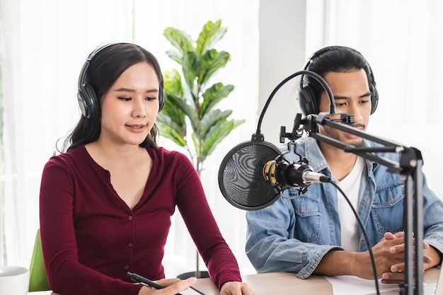 Lächeln zwei asiatische junge frau, mann radiomoderatoren in kopfhörern, mikrofon beim sprechen, konversation, aufnahme von podcast im rundfunk im studio zusammen. Technologie zur Erstellung von Audiokonzepten.