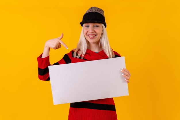 Lächelnd auf ein leeres Werbeplakat zeigen Blondes kaukasisches Mädchen auf gelbem Hintergrundstudio