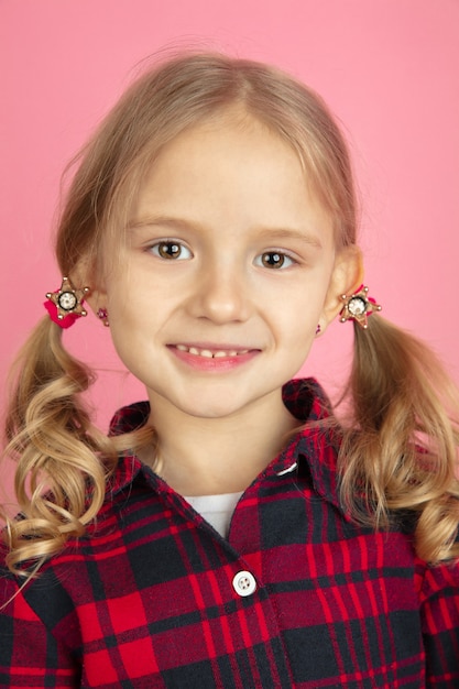 Lächelnd. Nahaufnahme Porträt des kaukasischen kleinen Mädchens auf rosa Wand. Schönes weibliches Modell mit blonden Haaren.