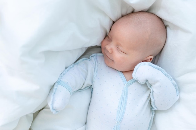 Lächelnd oder lachend in einem Traum schläft ein neugeborener Junge sieben Tage lang in einem Kinderbett zu Hause auf einem Baumwollbett in der Nähe