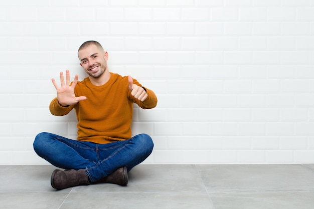 lächelnd und freundlich aussehend, Nummer sechs oder sechst mit der Hand nach vorne zeigend, Countdown