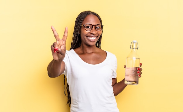 Lächelnd und glücklich aussehend, unbeschwert und positiv, mit einer Hand Sieg oder Frieden gestikulieren. Wasserflaschenkonzept