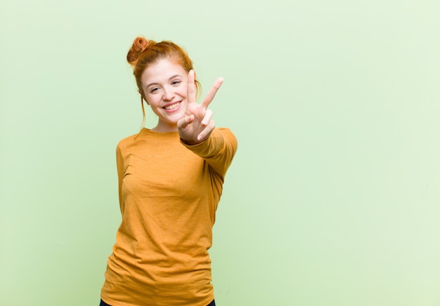 lächelnd und glücklich, sorglos und positiv aussehend, Sieg oder Frieden mit einer Hand gestikulierend