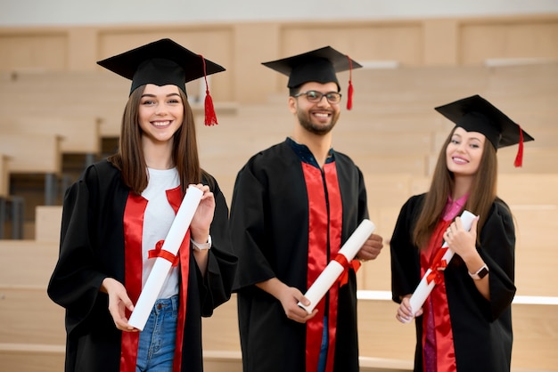 Lächelnde Absolvent, die Diplome vor hölzernen Schreibtischen halten.