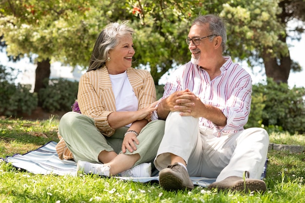 Lächelnde ältere europäische mann und frau sitzen auf plaid genießen romantisches date picknick im park haben spaß