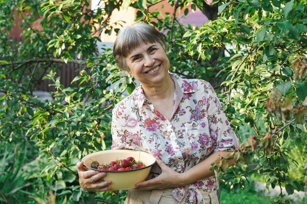 Lächelnde ältere Frau, die eine Schüssel mit frischen Erdbeeren in den Händen hält