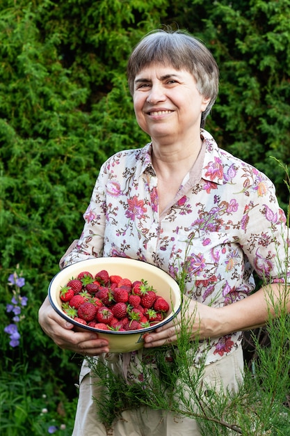 Lächelnde ältere Frau, die eine Schüssel mit frischen Erdbeeren in den Händen hält