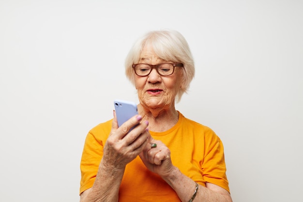 Lächelnde ältere Frau in einem gelben T-Shirt, die Kommunikation per Telefon in Nahaufnahme aufwirft