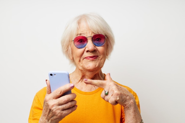 Lächelnde ältere Frau in modischer Brille mit hellem Hintergrund eines Smartphones in der Hand