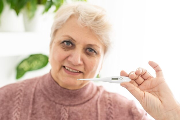 Lächelnde ältere Frau zeigt Thermometer.