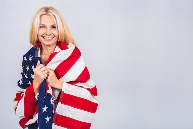 Lächelnde ältere schöne patriotische Frau, die Flagge der Vereinigten Staaten trägt lokalisiert über weißem Hintergrund mit einem Überraschungsgesicht.