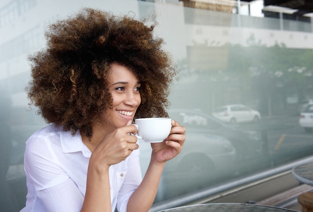 Lächelnde Afroamerikanerfrau, die mit Tasse Kaffee sitzt