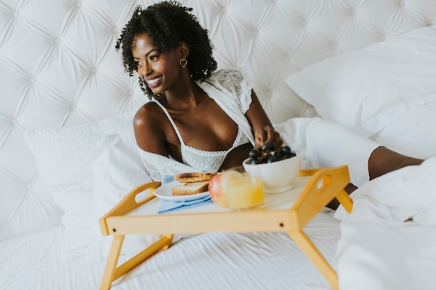 Lächelnde Afroamerikanerfrau, die zu Hause ein entspannendes Frühstück im Bett hat