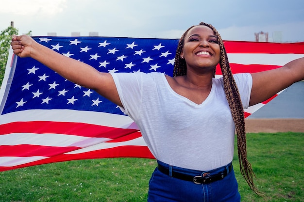 Lächelnde afroamerikanische Frau mit USA-Flagge und Blick in die Kamera Herbstabend Frühling im Park am See