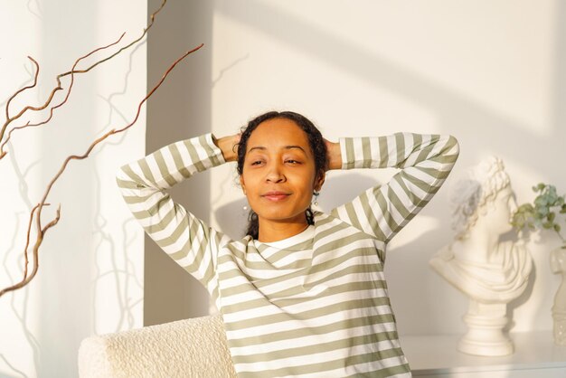 Foto lächelnde afroamerikanische frau schaut durch das fenster und genießt das natürliche licht des sonnenuntergangs.