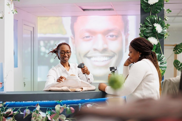 Lächelnde afroamerikanische Kassiererin scannt Kundenkleidung an der Kasse. Frau steht am Schalter und wartet darauf, den Einkauf zu bezahlen, während der Mitarbeiter Kassenterminal und Scanner benutzt
