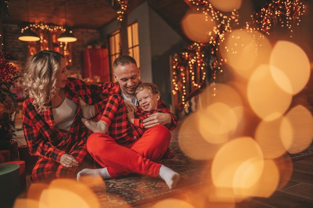 Foto lächelnde aktive eltern mit kleinen söhnen in roten gerahmten schlafanzügen warten auf den weihnachtsmann im haus