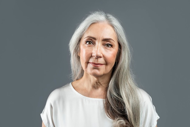Lächelnde alte europäische Frau mit grauem Haar, die isoliert auf grauem Hintergrundstudio in die Kamera blickt