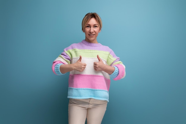 Lächelnde angenehme blonde junge Frau in einem gestreiften Pullover zeigt wie mit der Hand auf einem blauen