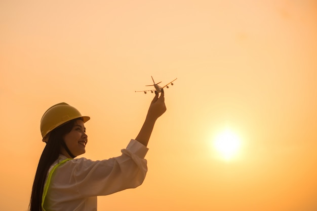 Lächelnde Angestelltfrau, die Flugzeug in den Händen mit Sonnenuntergang hält.