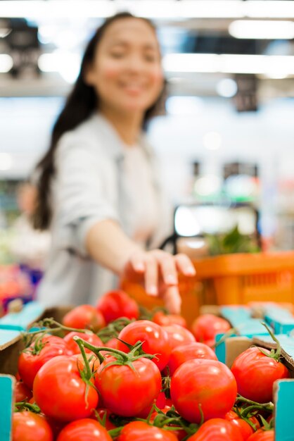 Lächelnde Asiatin, die Tomaten im Supermarkt wählt