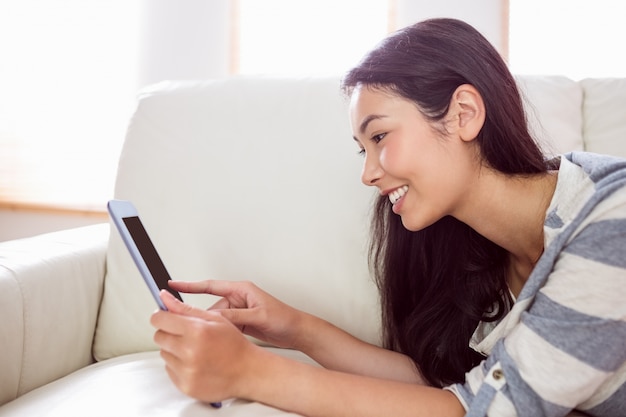 Lächelnde asiatische Frau auf Couch unter Verwendung der Tablette