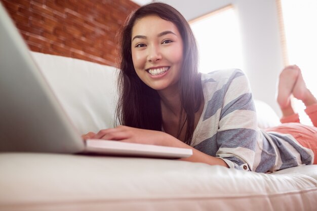 Lächelnde asiatische Frau auf Couch unter Verwendung des Laptops