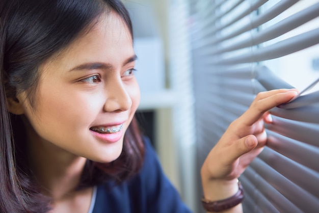 Lächelnde asiatische Frau, die aus dem Fenster des Büros schaut.